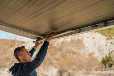 Ein Mann klappt den Stützfuß einer Fiamma F45s Markise manuell in das Gehäuse ein