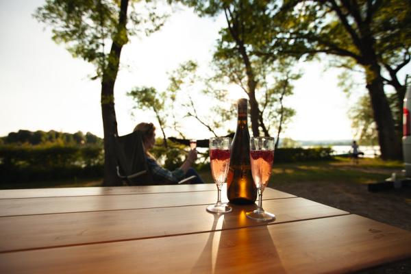 Bambustisch von HOLIDAY TRAVEL im Abendlicht, mit Sektgläsern und Flasche, aufgebaut auf dem Campingplatz.
