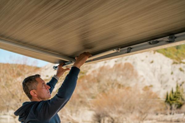 Ein Mann klappt den Stützfuß einer Fiamma F45s Markise manuell in das Gehäuse ein