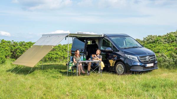 Outwell Hillcrest Tarp am Mercedes-Van, grün gespannt, zwei Personen sitzen darunter auf Campingstühlen im Gras