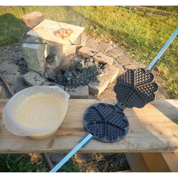 Origin Outdoors Waffeleisen geöffnet auf Campingtisch, daneben ein Teigtopf für die Zubereitung sichtbar platziert.